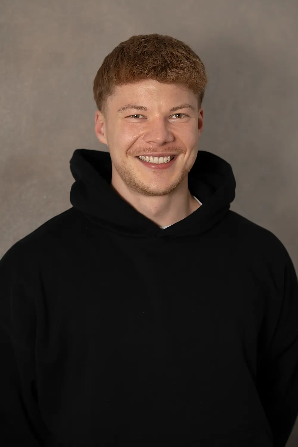 Portrait eines männlichen Trainers im schwarzen Hoodie im Fitnessstudio Body & Soul in Billerbeck, freundlicher Blick in die Kamera.