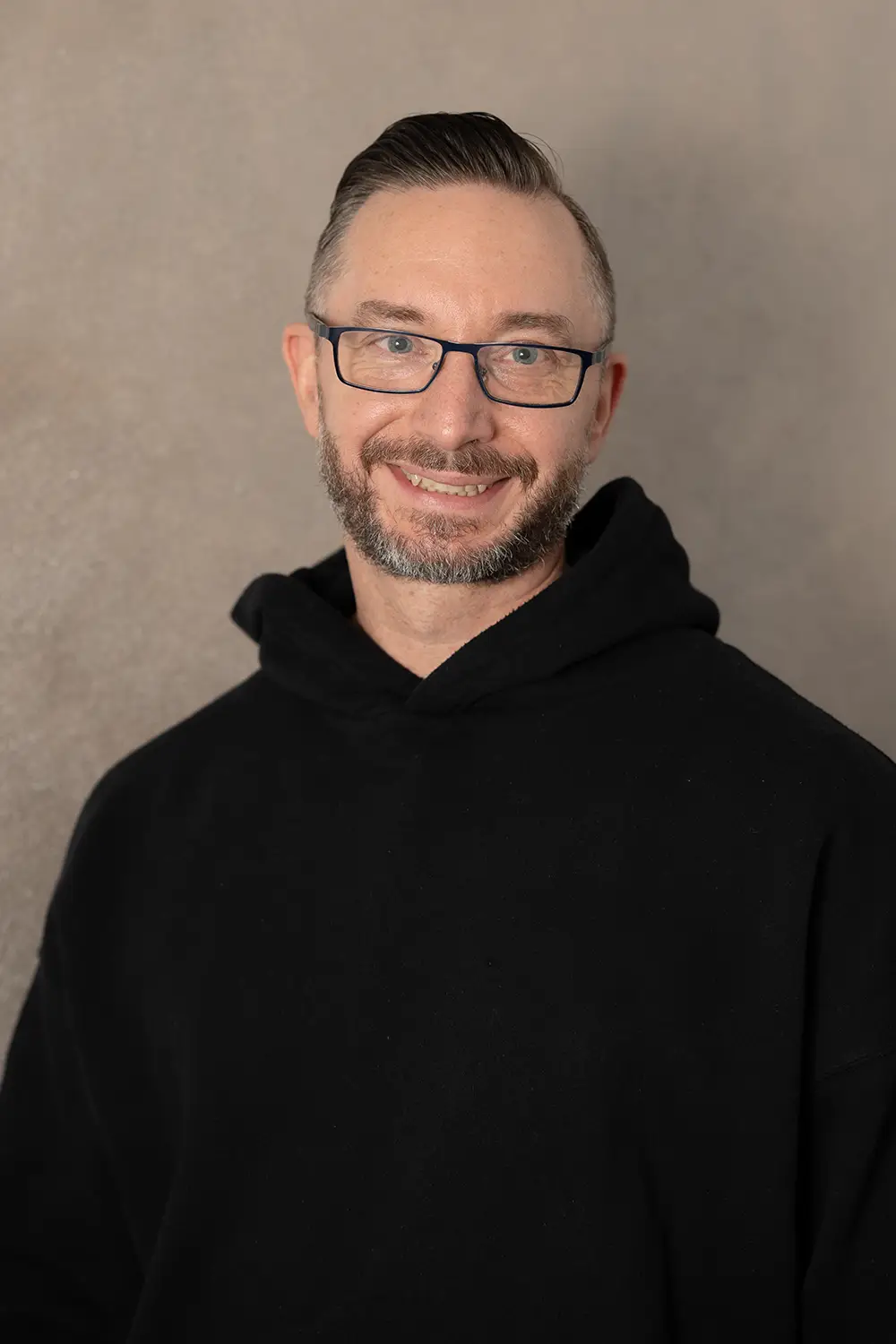 Portrait eines männlichen Trainers im schwarzen Hoodie im Fitnessstudio Body & Soul in Billerbeck, freundlicher Blick in die Kamera.