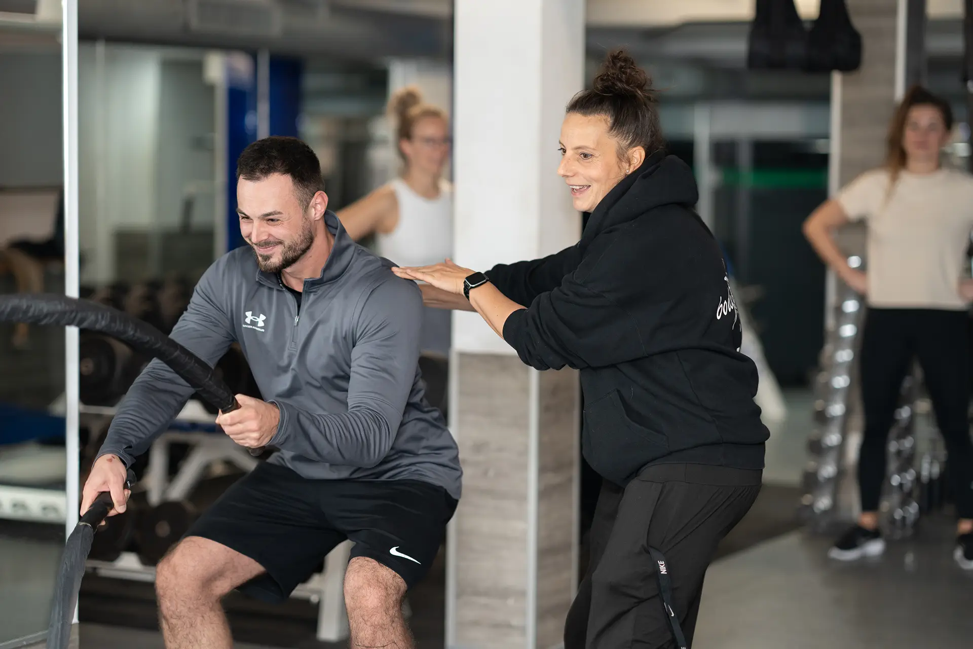 Trainerin unterstützt einen Mann beim funktionellen Seiltraining im Fitnessstudio body & soul Billerbeck, während weitere Mitglieder im Hintergrund trainieren