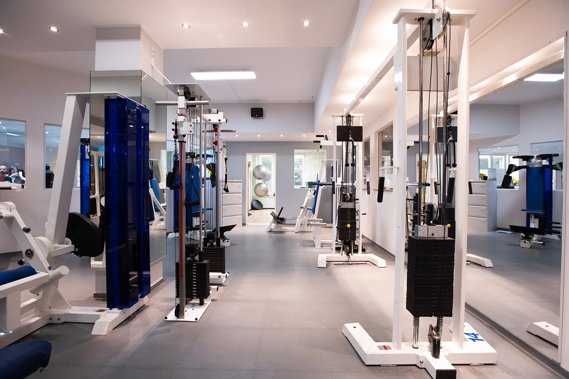 Heller und moderner Trainingsbereich im Fitnessstudio mit verschiedenen Kraftgeräten, Seilzugstationen und Spiegelwänden in aufgeräumter, professioneller Umgebung