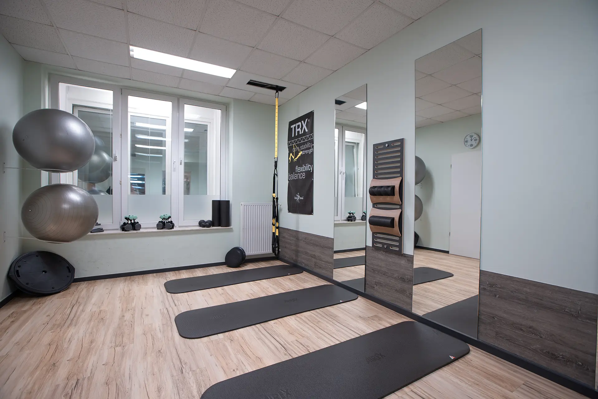 Heller Functional-Training-Raum mit TRX-Band an der Decke, mehreren Trainingsmatten auf dem Boden, großen Spiegeln an der Wand und Gymnastikbällen im Hintergrund