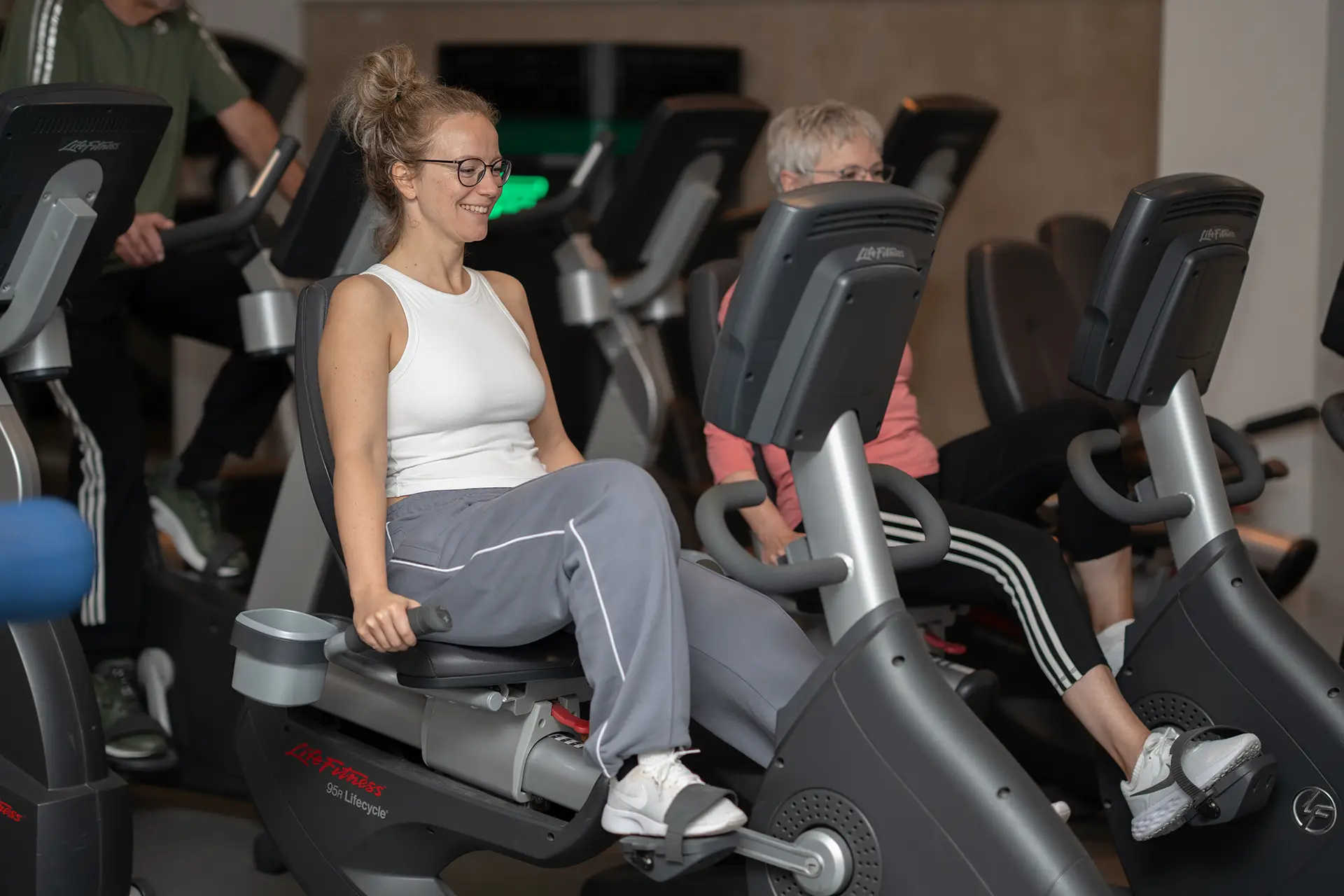 Frau trainiert auf einem Sitz-Ergometer im Fitnessstudio body & soul Billerbeck, weitere Mitglieder nutzen Ausdauergeräte im Hintergrund