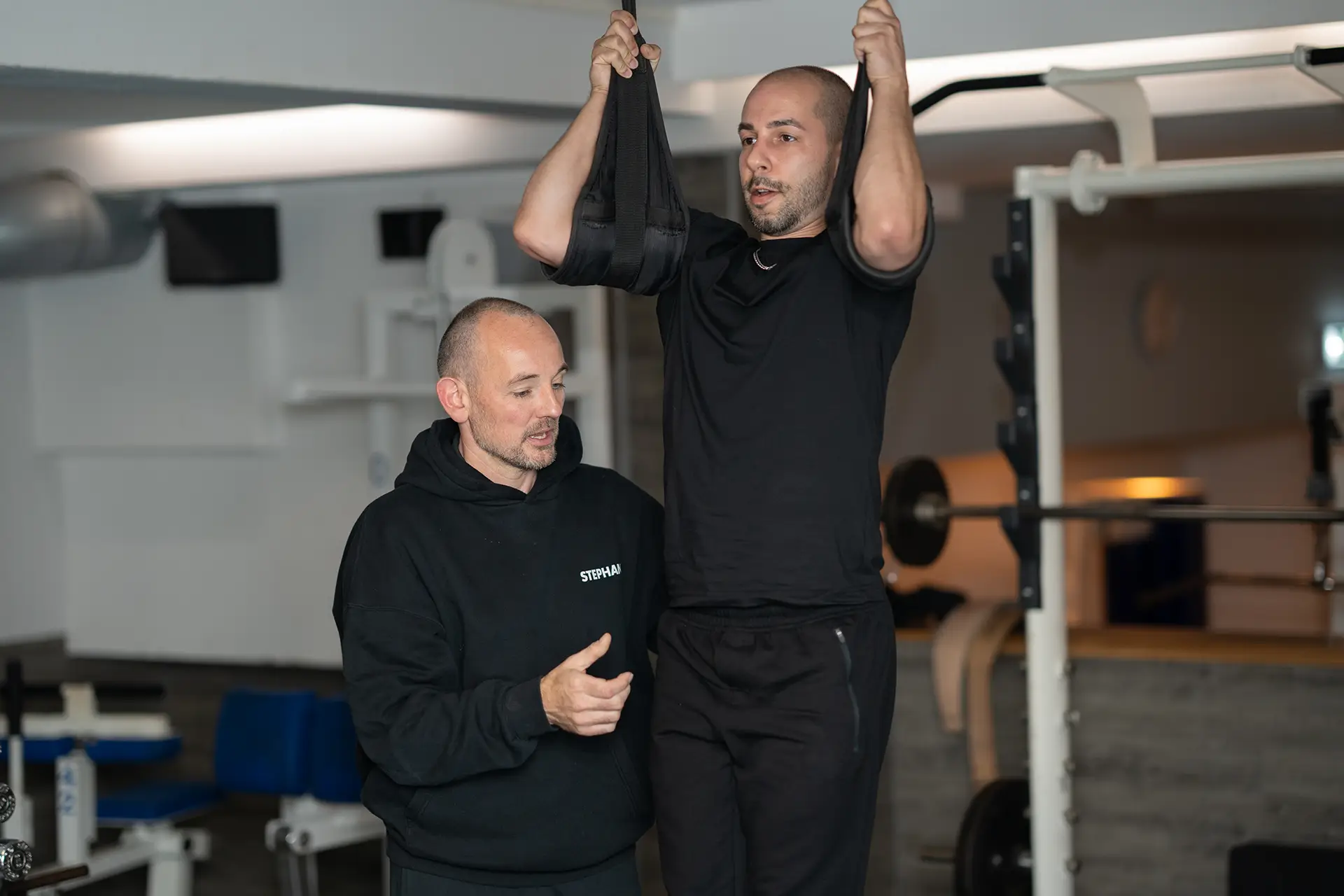 Trainer begleitet einen Mann bei einer geführten Zugübung mit Trainingsschlaufen im Fitnessstudio body & soul Billerbeck und gibt Hinweise zur richtigen Ausführung