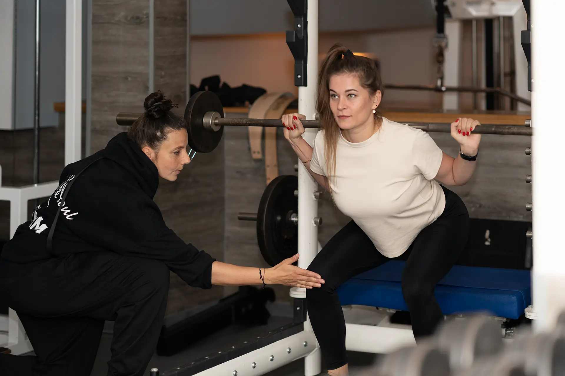 Trainerin korrigiert die Knieposition einer Frau bei einer geführten Kniebeuge mit Langhantel im Fitnessstudio body & soul Billerbeck