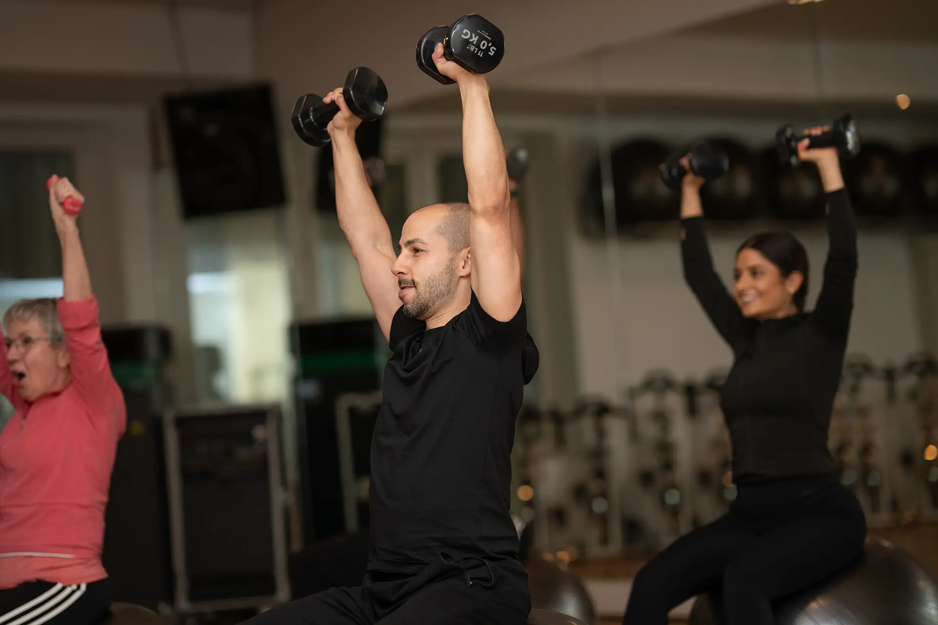 Gruppe trainiert mit Kurzhanteln in einem Kursraum im Fitnessstudio body & soul Billerbeck, Trainer führt die Übung in der Mitte an