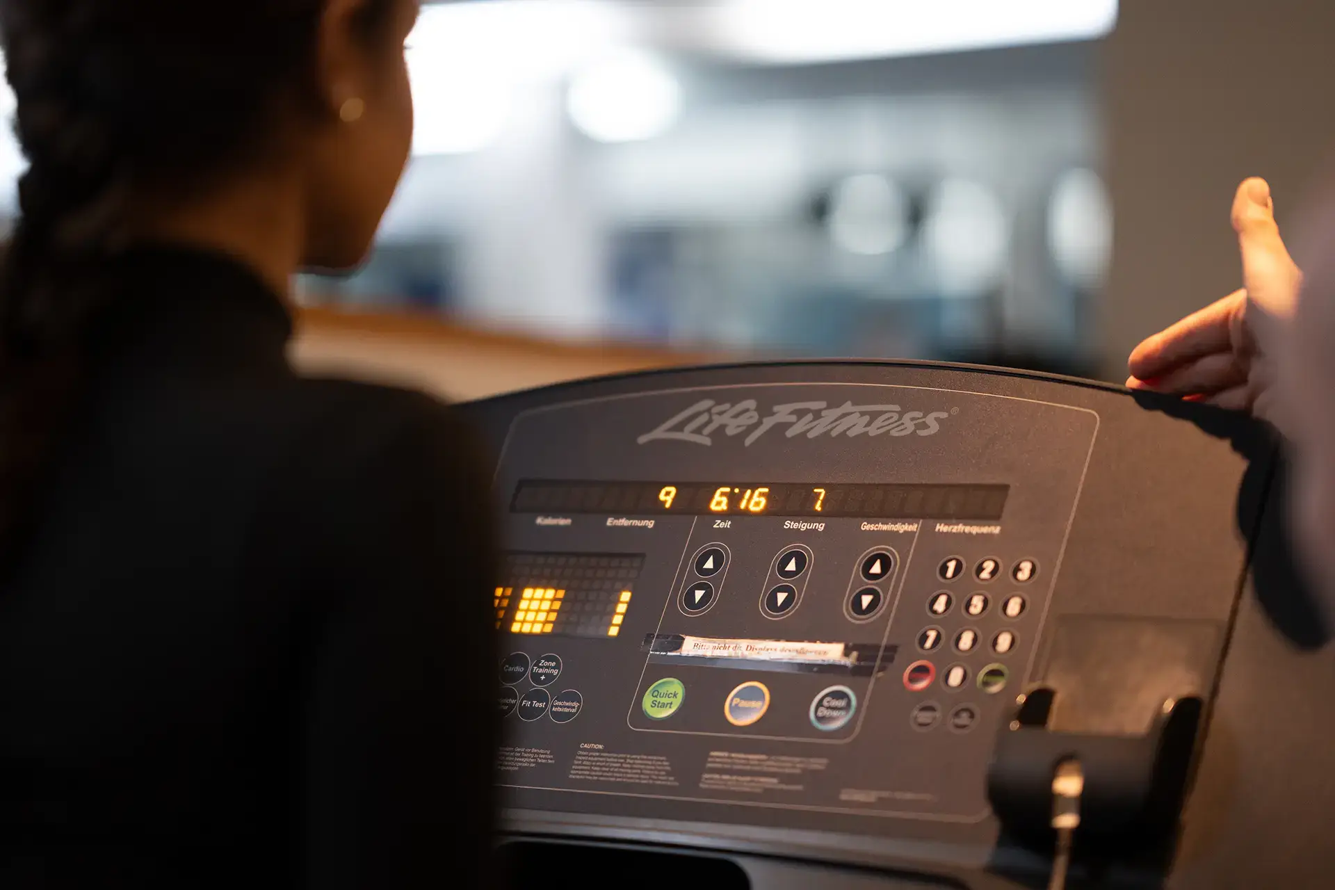 Person nutzt ein Laufband mit Bedienfeld im Cardio-Bereich des Fitnessstudios Body & Soul in Billerbeck, Anzeige für Zeit, Distanz und Steigung ist sichtbar, Trainerhand gibt ein positives Zeichen.
