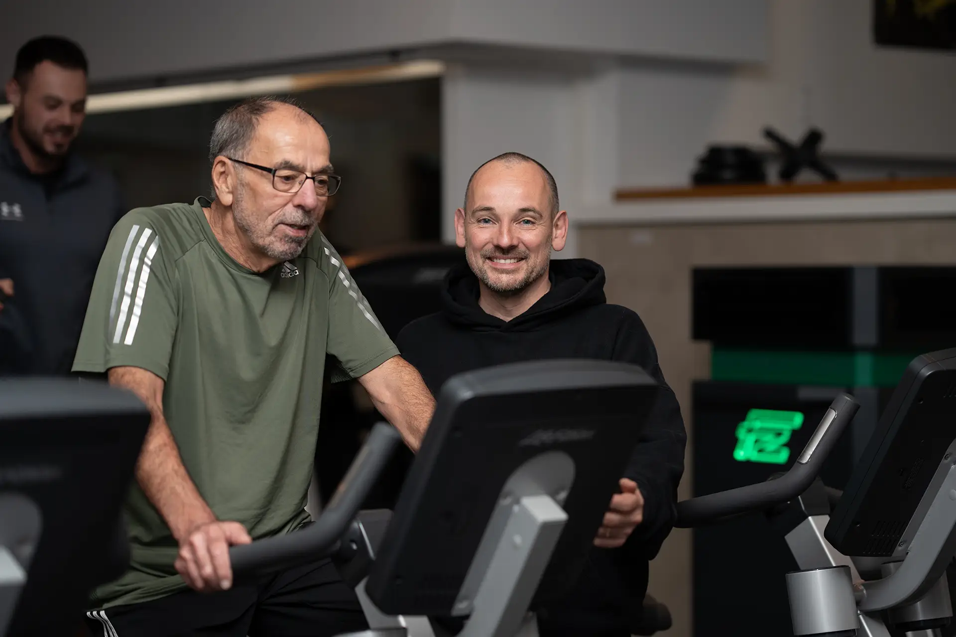 Trainer begleitet einen Mann beim Training auf einem Ausdauergerät im Fitnessstudio body & soul Billerbeck und erklärt die Anzeige des Geräts