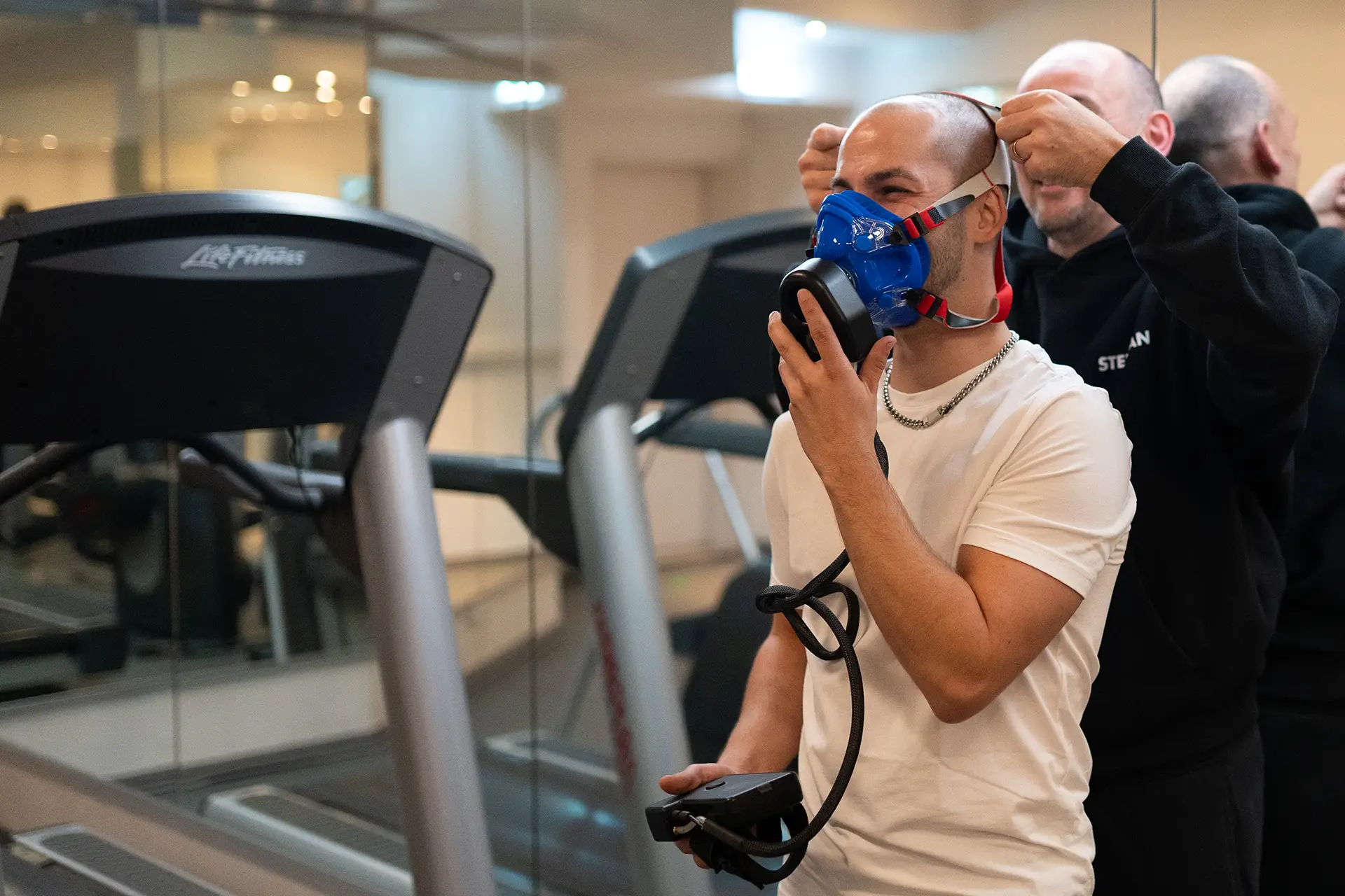 Trainer passt einer Person die Atemmaske für eine Leistungsdiagnostik auf dem Laufband im Fitnessstudio body & soul Billerbeck an