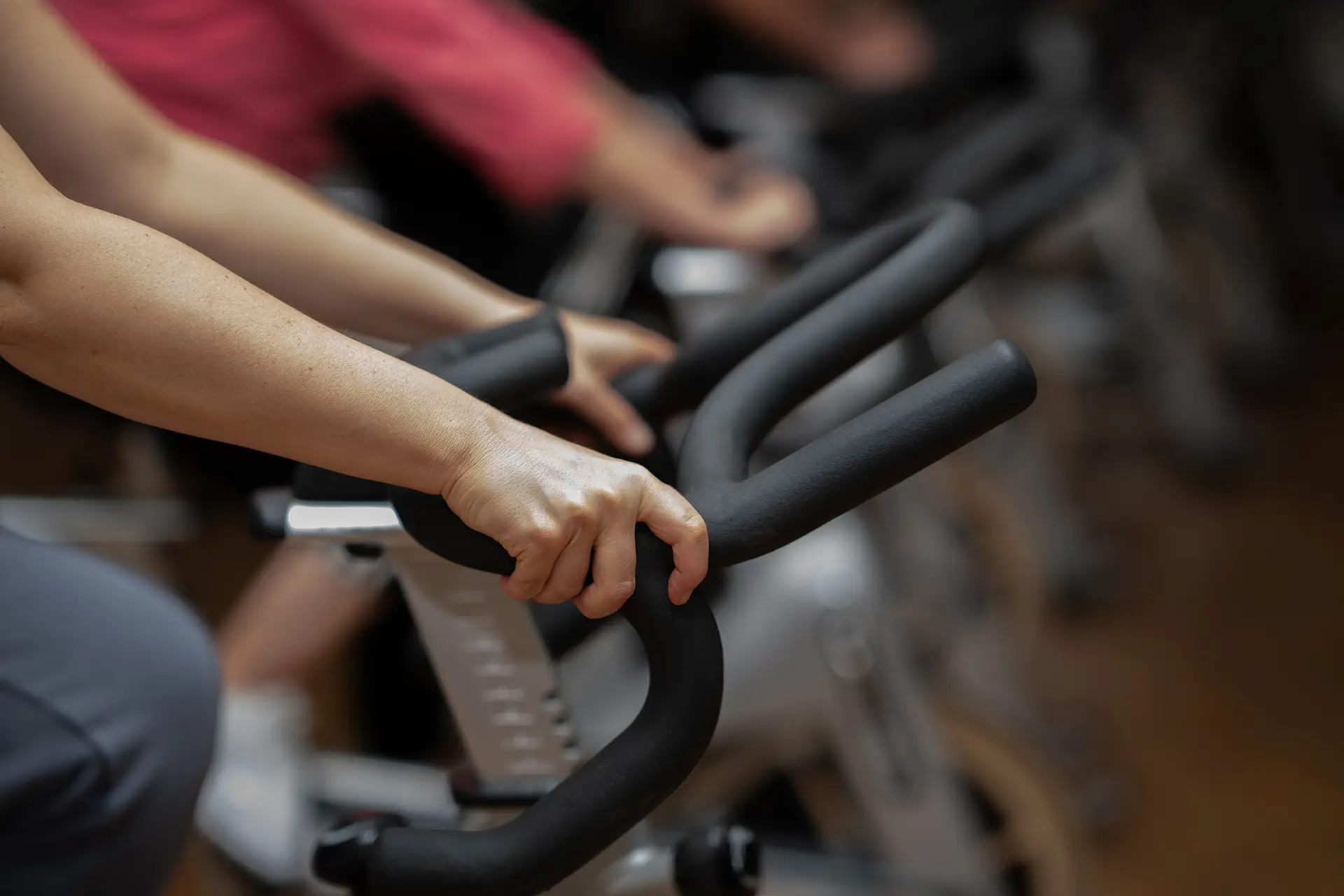 Hände greifen die Lenker eines Indoor-Bikes während eines Gruppentrainings im Fitnessstudio body & soul Billerbeck