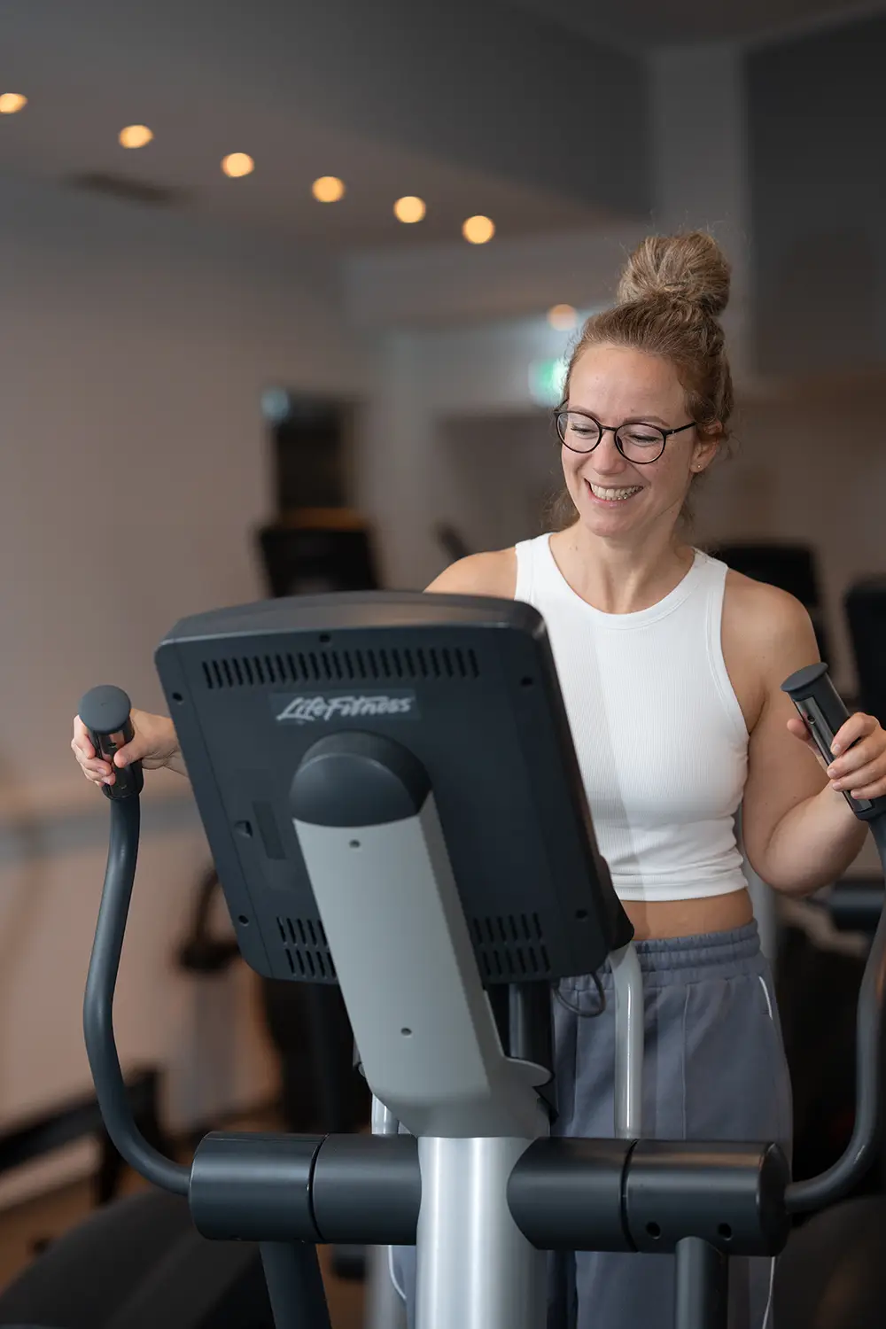 Frau trainiert lächelnd an einem Crosstrainer im Fitnessstudio body & soul Billerbeck und schaut auf das Display des Geräts